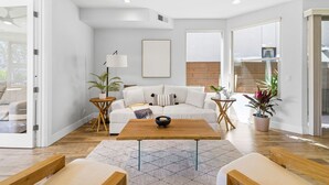 Ein modernes Wohnzimmer mit Couchtisch aus Holz, einer weißen Couch und einem großen Fenster.