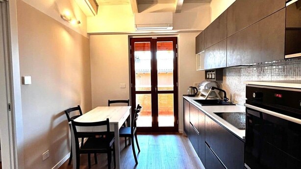 A modern kitchen with a dining area, wooden flooring, and a view through a glass door. - Casa Paolina Apartment - Lomazzo (Lomazzo)