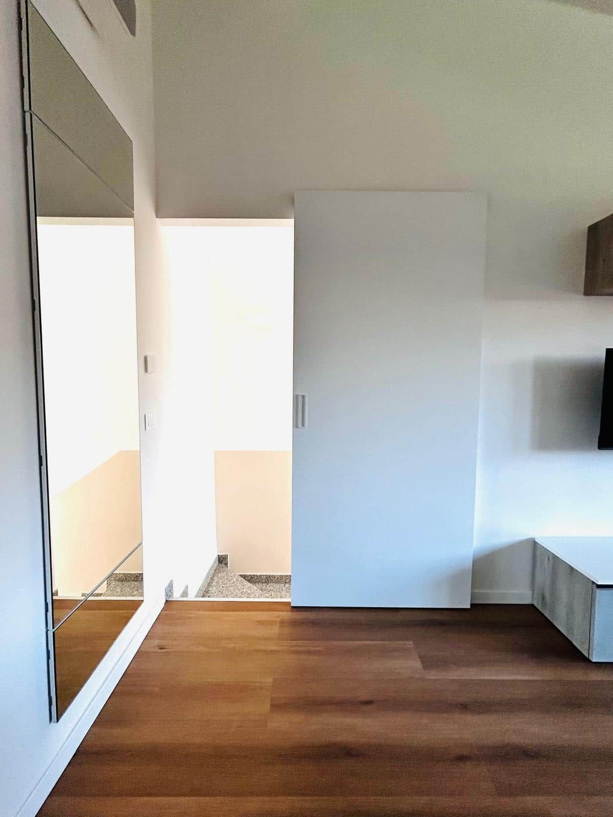 Ein modernes Interieur mit Holzboden, einer weißen Tür und einer sichtbaren Treppe.