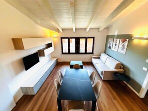 A modern living room with a wooden ceiling, built-in TV, sofa, dining table, and artwork on the walls. - Casa Paolina Apartment - Lomazzo (Lomazzo)