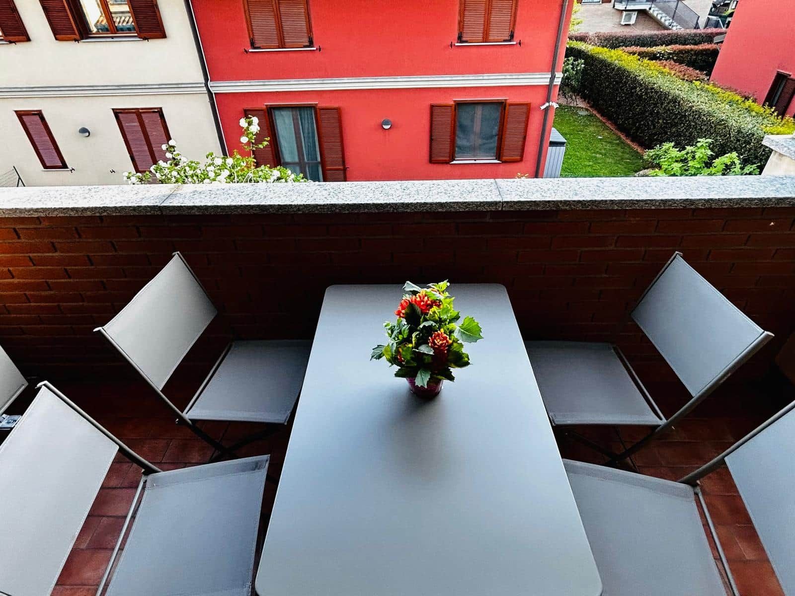 Un balcon avec une table et des chaises, un pot de fleurs et une vue sur un immeuble rouge.
