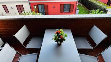 Un balcon avec une table et des chaises, un pot de fleurs et une vue sur un immeuble rouge.