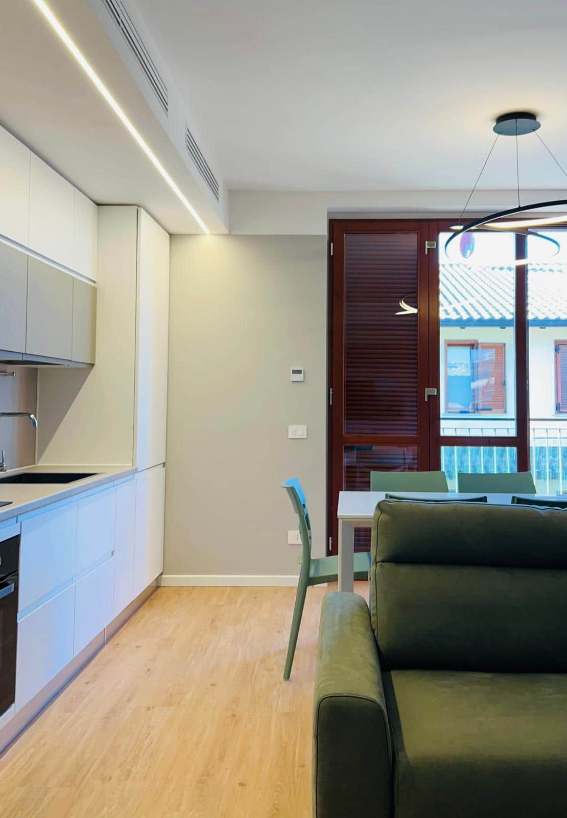 Een moderne keuken met witte kastjes, een ingebouwde kookplaat en een zithoek met een groene bank en een tafel.