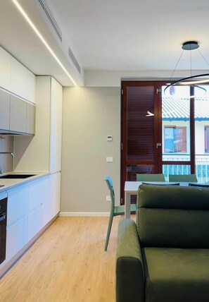 Een moderne keuken met witte kastjes, een ingebouwde kookplaat en een zithoek met een groene bank en een tafel.