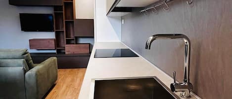 A modern kitchen with a built-in stainless steel sink, wooden shelves, and a flat-screen TV mounted on the wall.