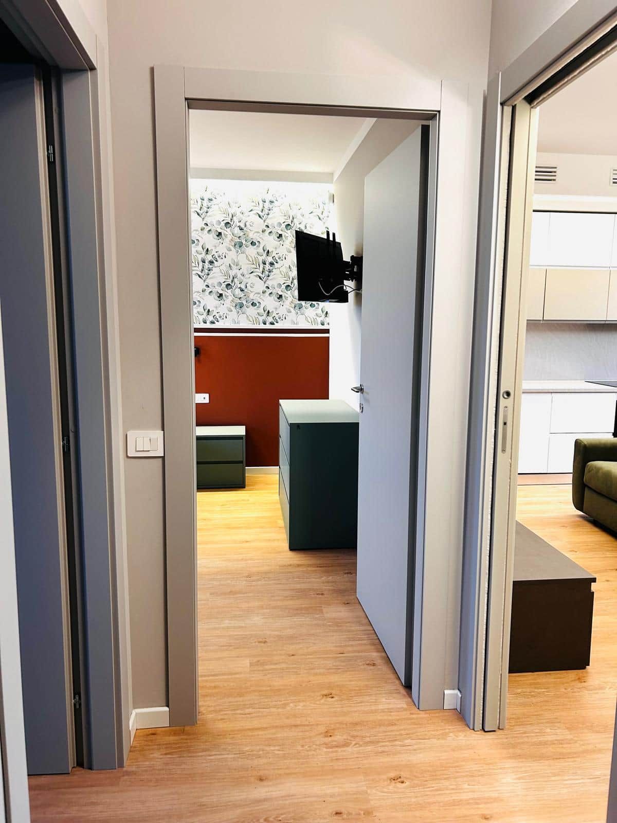 A modern apartment with a wooden floor, a kitchen area with white cabinets, and a living space with a sofa.