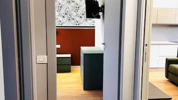 A modern apartment with a wooden floor, a kitchen area with white cabinets, and a living space with a sofa.
