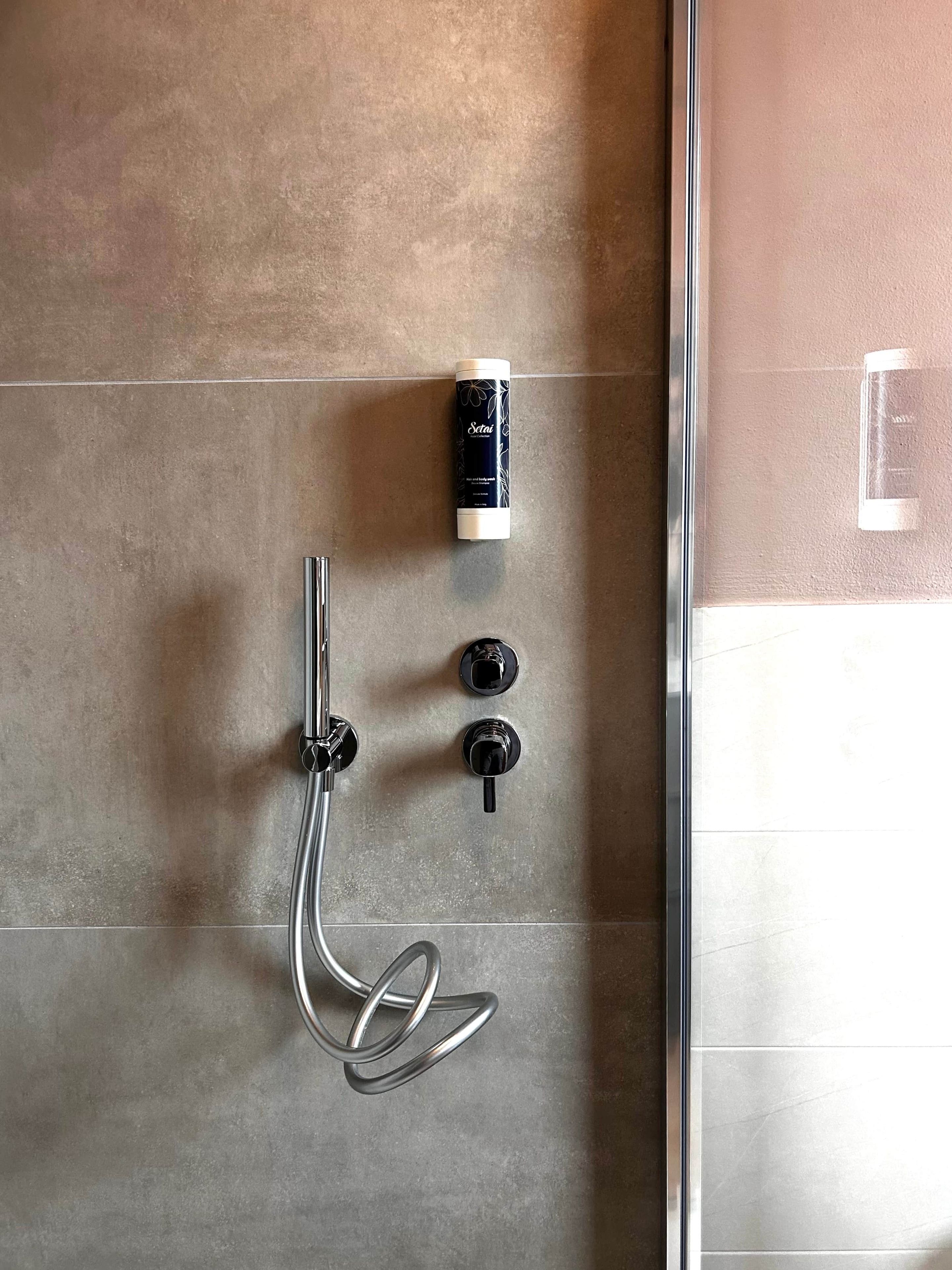 Une douche équipée d’un pommeau de douche à main, d’un panneau de commande avec deux boutons et d’une bouteille de shampoing.