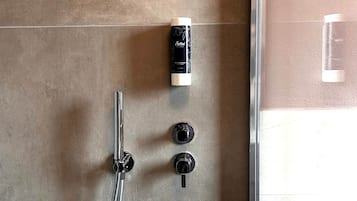 Une douche équipée d’un pommeau de douche à main, d’un panneau de commande avec deux boutons et d’une bouteille de shampoing.