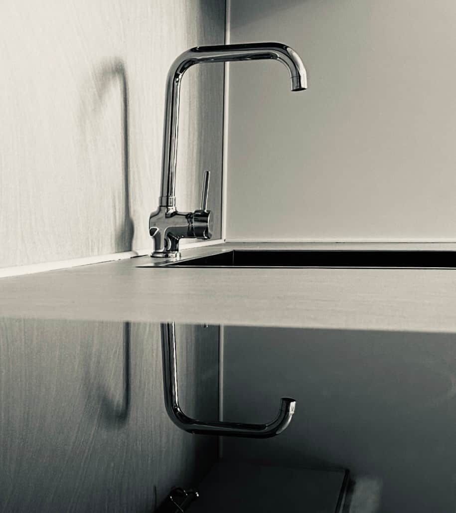 Une salle de bain moderne, dotée d’un robinet élégant en métal et d’un plan de toilette réfléchissant.