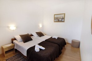 A hotel room with two beds, a nightstand, a small round ottoman, and a painting on the wall. - Spacious Apartment in Umag (Umag)