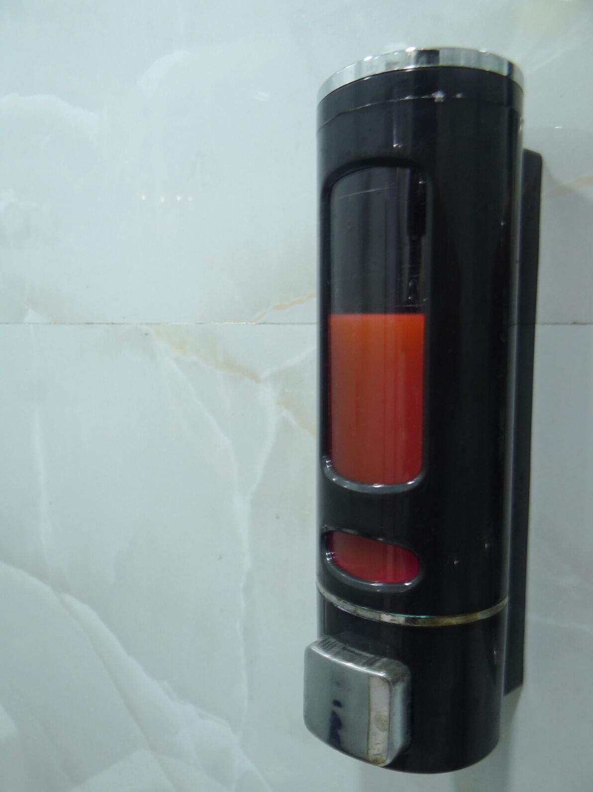 A black, cylindrical object with a metallic base, mounted on a wall with a white, marble-like texture.