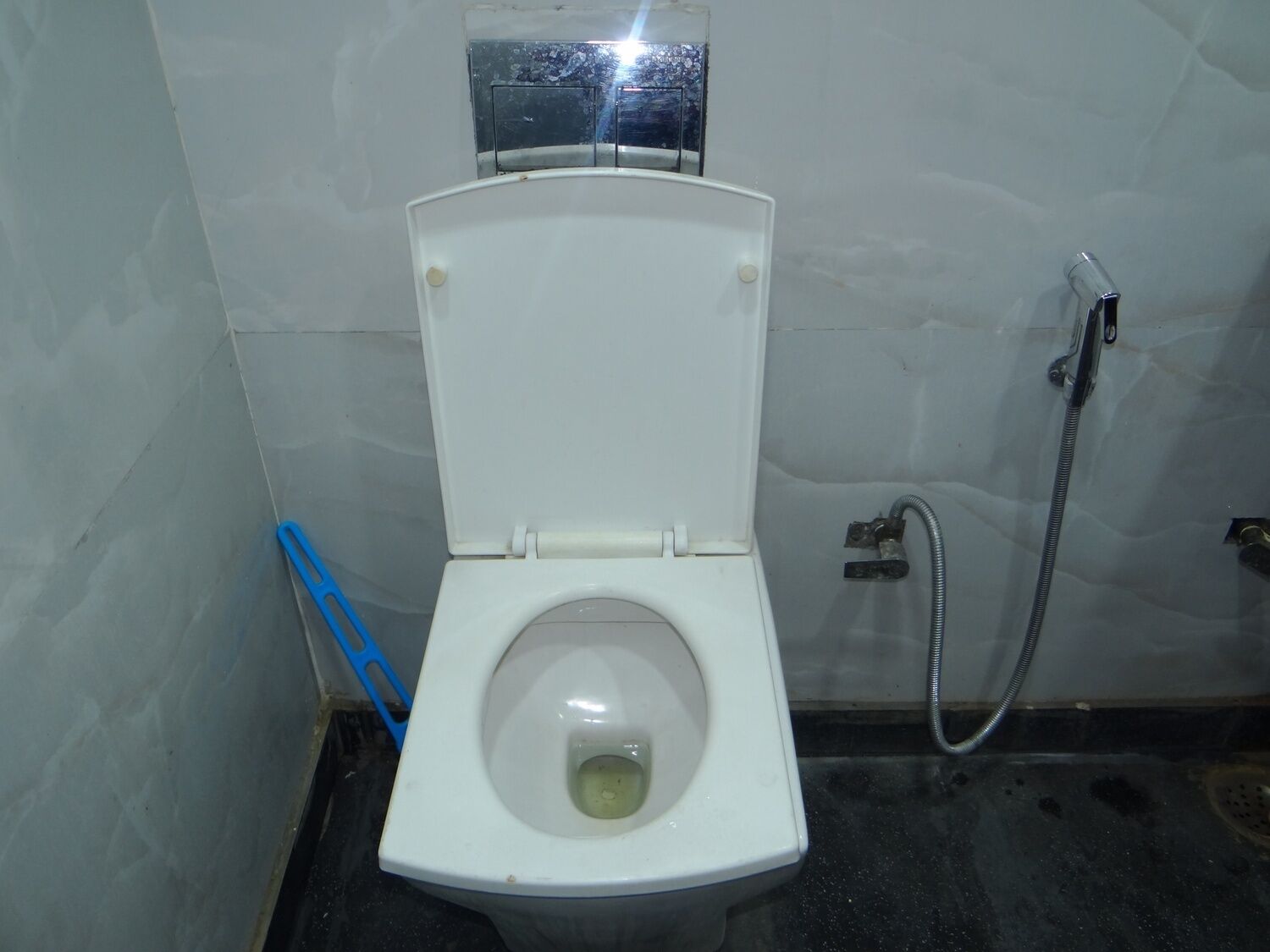 Um vaso sanitário branco com a tampa fechada, um chuveiro e um banquinho de plástico azul ao lado.