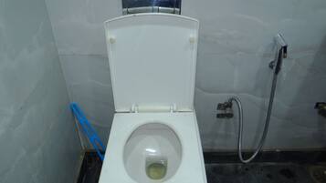 Um vaso sanitário branco com a tampa fechada, um chuveiro e um banquinho de plástico azul ao lado.