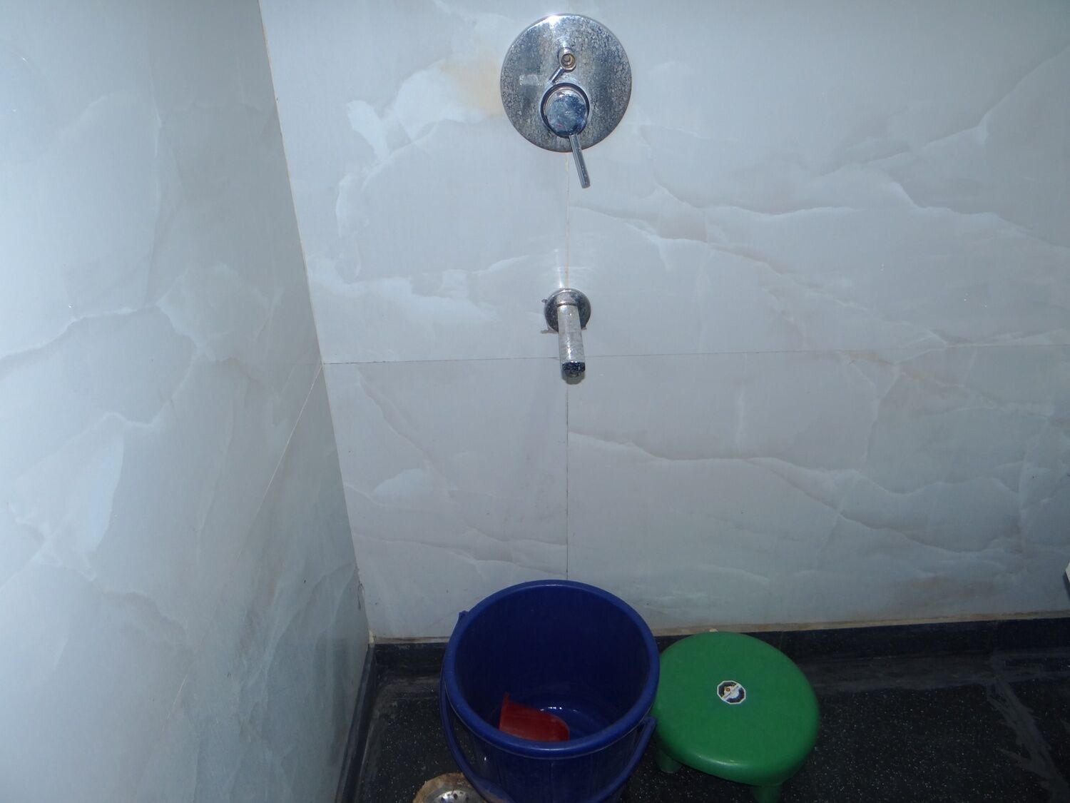 A bathroom with white marble tiles, a blue bucket, and a green stool.