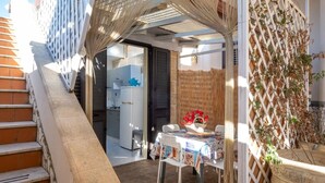 A patio area with a table set for dining, a refrigerator in the background, and a staircase leading to an upper level. - Elegant Ground-floor Apartment in Porto Cesareo Design Moderno Vicino al Mare (Porto Cesareo)
