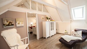 Quarto estilo loft com teto alto, vigas de madeira, uma poltrona de balanço branca, um sofá marrom e um armário com portas de vidro.