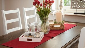 Uma mesa de jantar com um vaso de tulipas vermelhas, uma vela e saleiro e pimenteiro sobre um jogo americano vermelho.