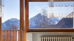 Habitación con vista a montañas nevadas a través de una ventana, un radiador y una puerta de madera con paneles decorativos.