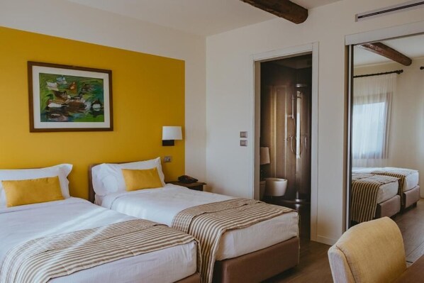 A hotel room with two beds, a yellow wall, a painting, a mirror, and a wooden ceiling beam.