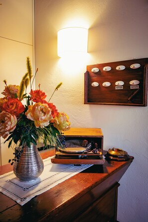 A wooden table with a vase of flowers, a record player, and a wall-mounted light fixture. - LE VIGNE MOROSINA (Cessalto)