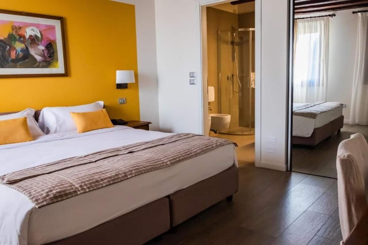 Habitación de hotel con una cama grande, zona de ducha y un pequeño rincón de descanso.