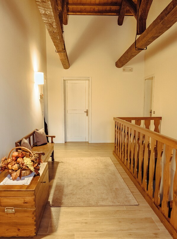 A hallway with a wooden bench, a basket of fruits, and a wooden chest. A door is visible in the background. - LE VIGNE MOROSINA (Cessalto)