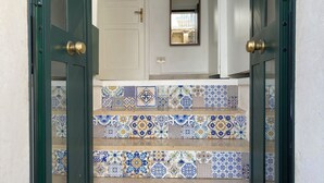 Una escalera con intrincados azulejos blancos y azules que lleva a una puerta blanca con picaporte de latón.