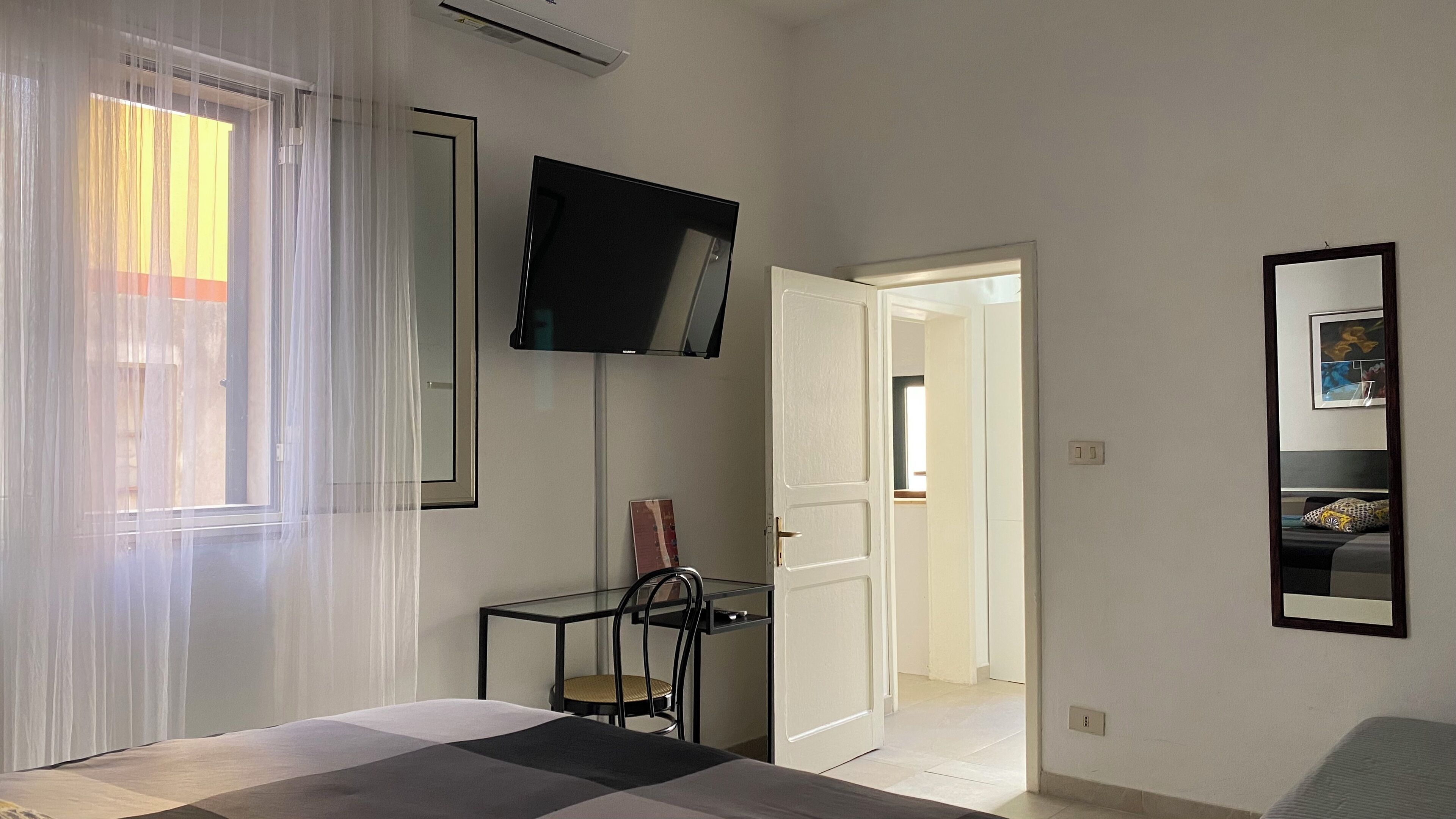 Ein Schlafzimmer mit einem Bett, einem an der Wand montierten Fernseher, einem Sessel und einer Tür zu einem anderen Raum.
