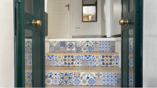 Una escalera con baldosas azules y blancas de diseño que conduce a una puerta con picaporte de latón.