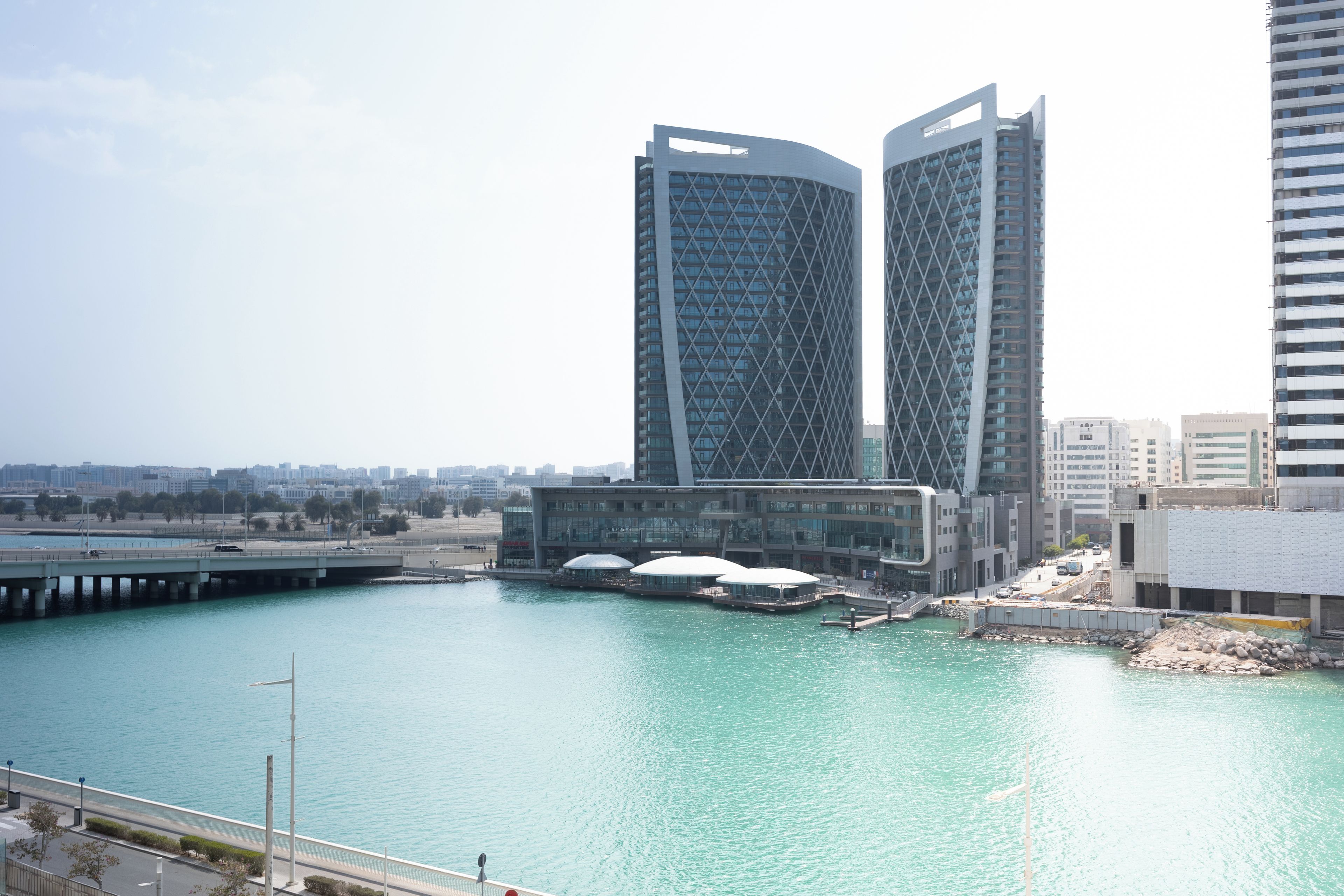 A waterfront view with modern buildings, a bridge, and a marina.