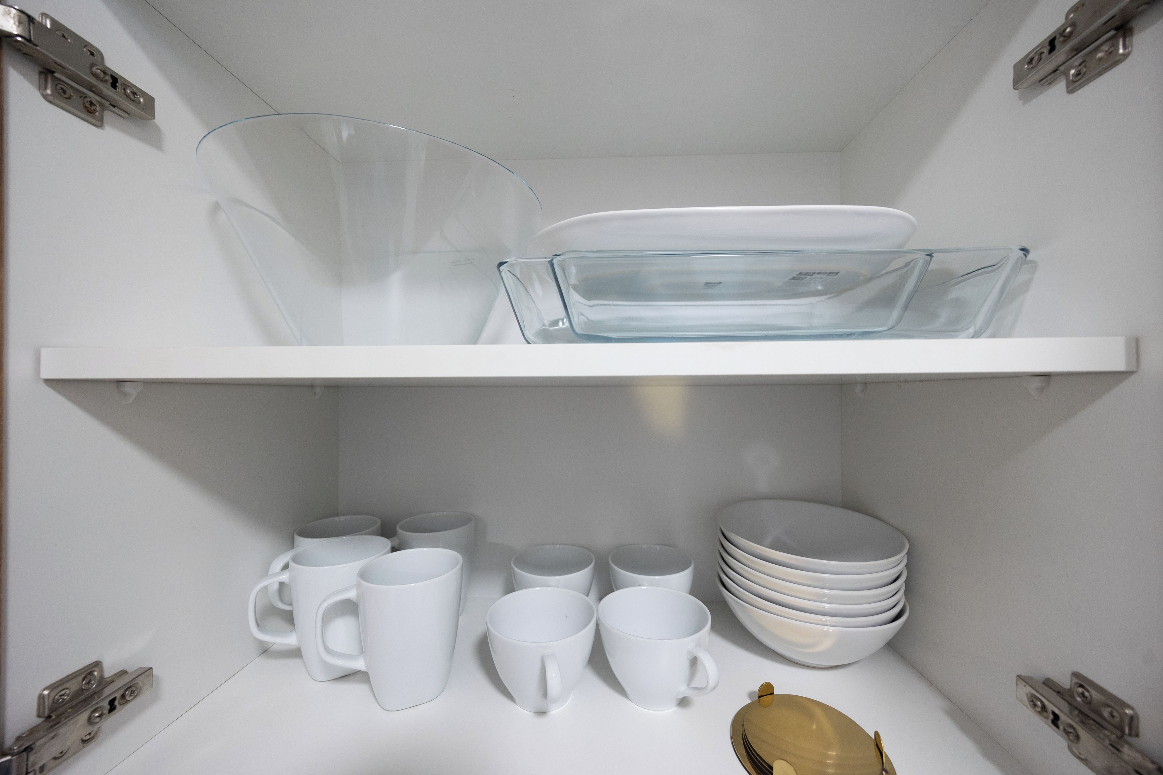 A kitchen with white cabinets, a glass dish rack, and white mugs and plates.