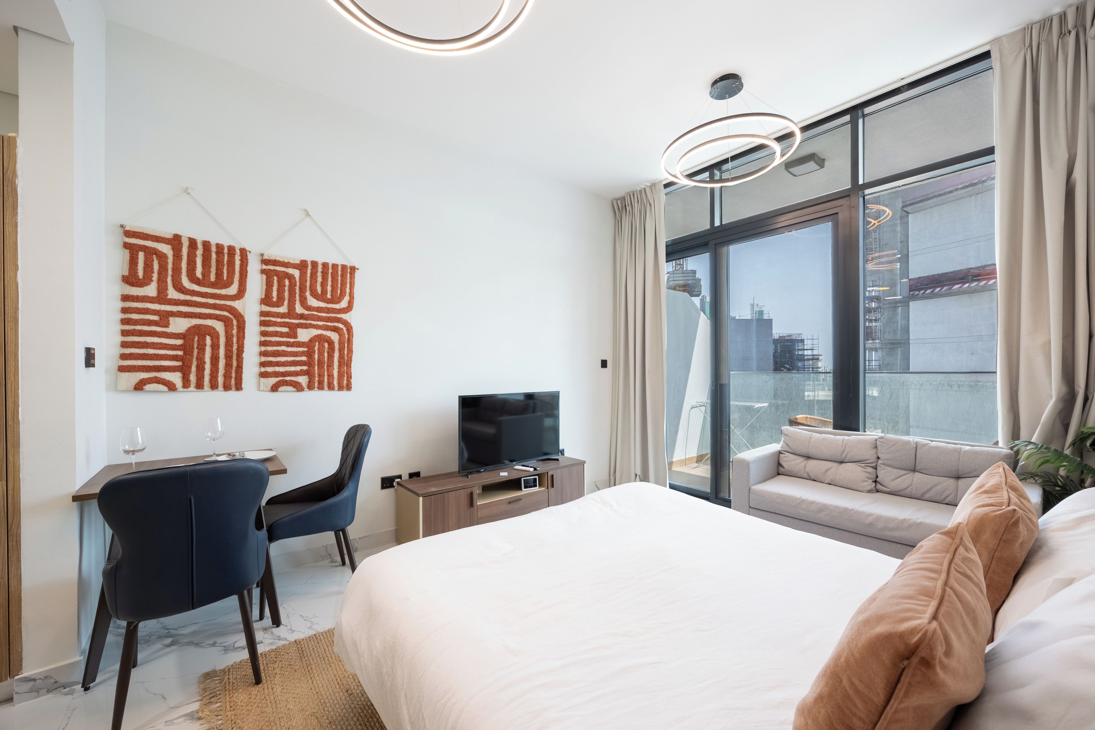 Ett modernt hotellrum med en stor säng, ett skrivbord med en stol, en tv och utsikt över staden genom stora fönster.