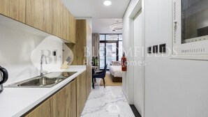 A modern kitchen with a marble countertop, wooden cabinets, and a stainless steel sink. - Elegance Stu Al Maryah Vista (Abu Dhabi)