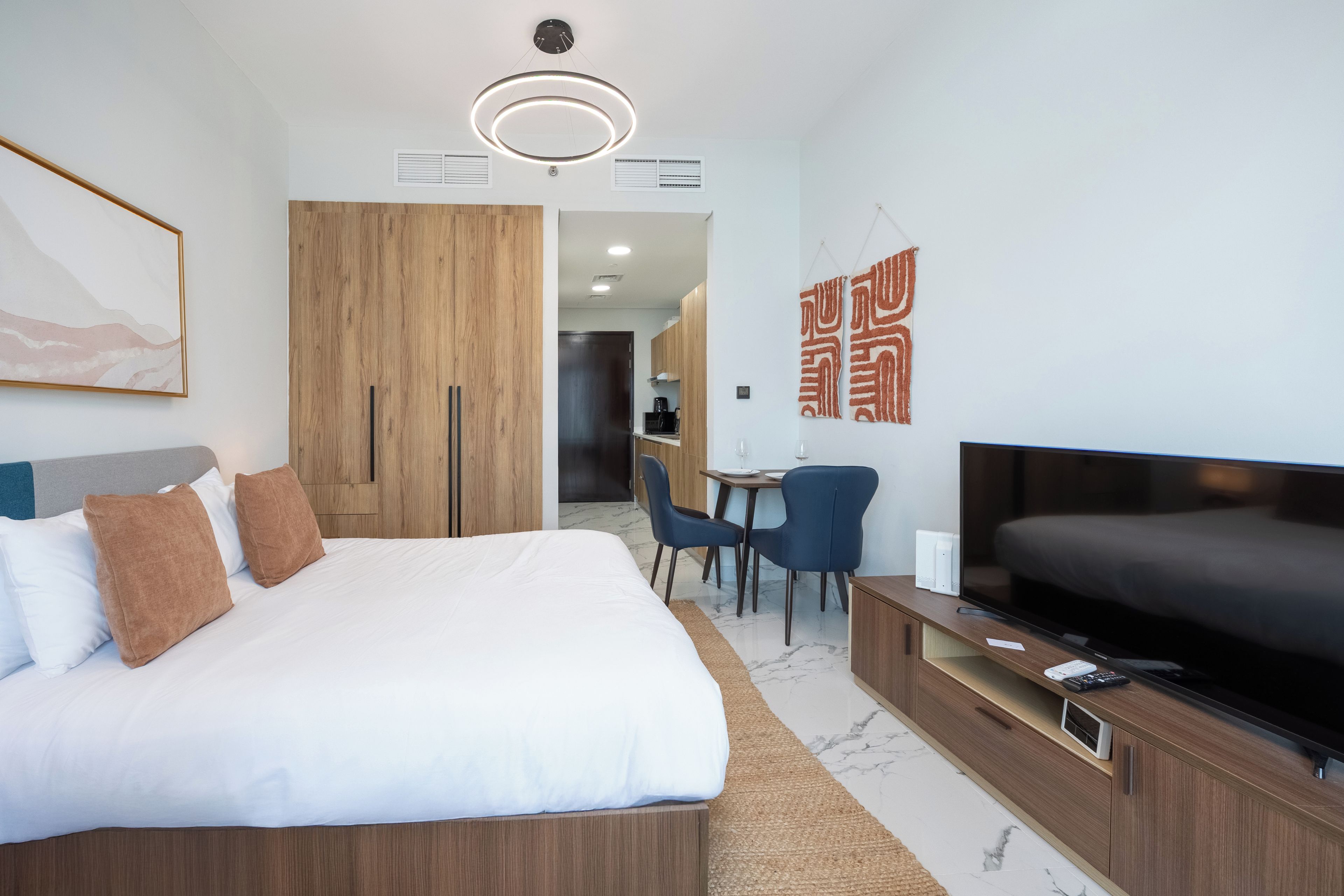 A modern hotel room with a large bed, a TV, a desk with chairs, and artwork on the walls.