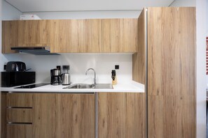 A modern kitchen with wooden cabinets, a stainless steel sink, a coffee maker, and a built-in range hood. - Elegance Stu Al Maryah Vista (Abu Dhabi)