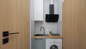 A compact kitchen with a washing machine, a sink, and a black range hood. - Cozy Studio for Two | Close to Metro | Pet-Friendly (Warszawa)