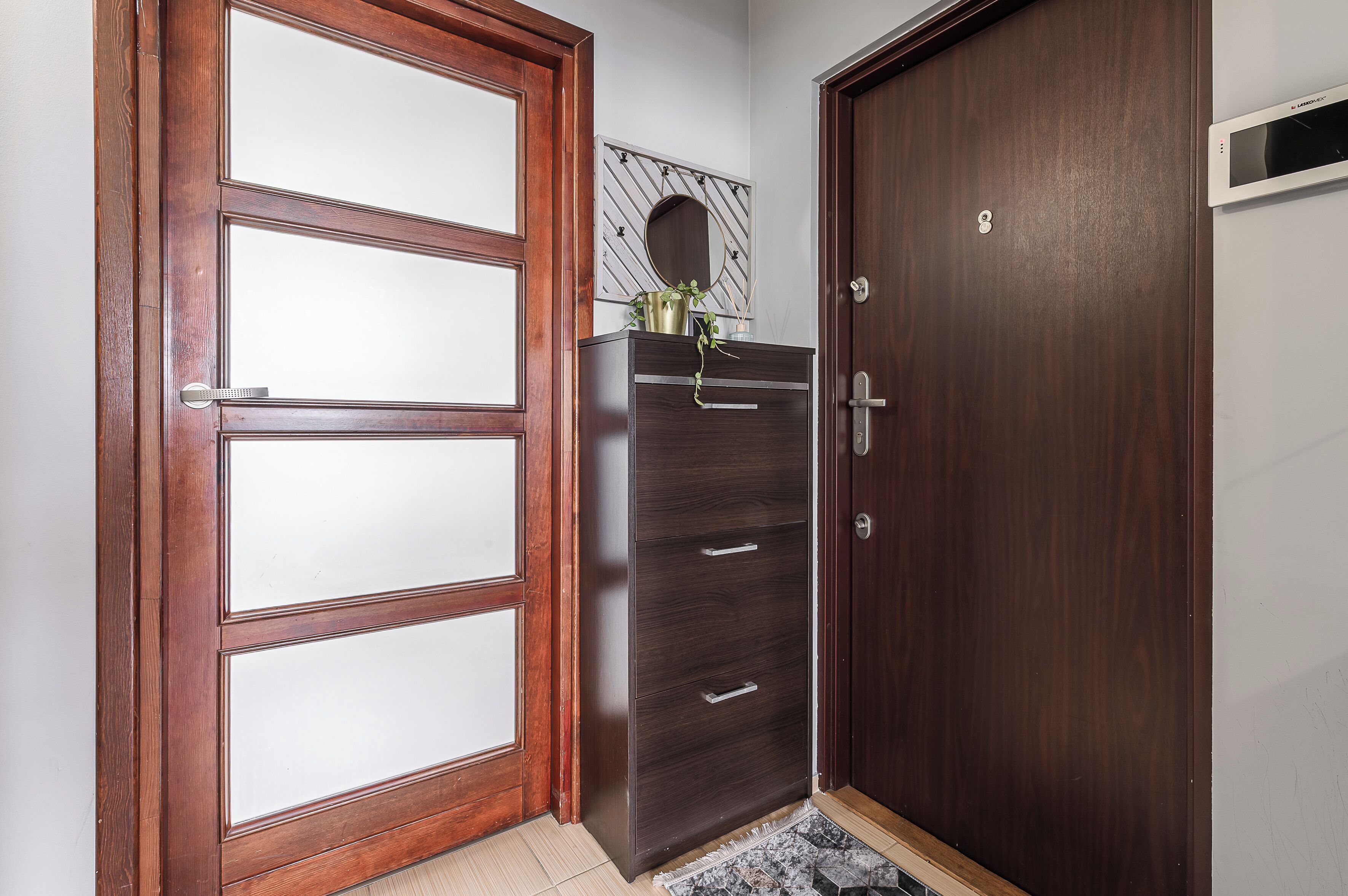 A wooden door with a glass panel, a dark wooden dresser with drawers, and a small mirror on the wall.