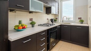 A modern kitchen with dark cabinets, a white countertop, a built-in stove, and a window with a city view. - Lumina 3-rooms apartment with parking (Warsaw)