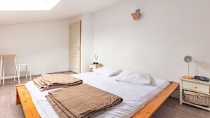 Un dormitorio con una cama, una mesita de noche, una lámpara, una silla y un tragaluz.