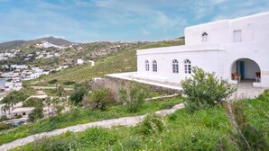 Un bâtiment blanc doté de fenêtres en arc de cercle et d’un portail, entouré de verdure et offrant une vue sur une colline.