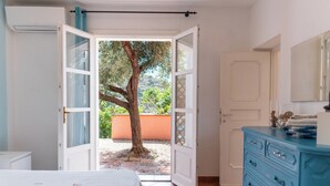 An open door leading to a balcony with a tree, a bed with a floral bedspread, and a blue dresser with drawers. - Sea walking distance, cozy apartment with garden, pets welcome (Pomonte)
