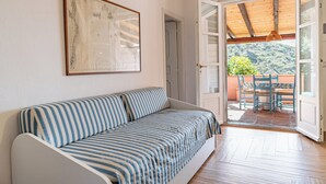 A room with a striped sofa, a framed picture on the wall, and an open door leading to a balcony with a wooden ceiling and a view of greenery. - Sea walking distance, cozy apartment with garden, pets welcome (Pomonte)