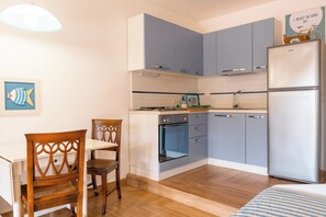 Eine kompakte Küche mit grauen Schränken, einem weißen Kühlschrank, einem Herd und einem Essbereich mit einem Holztisch und einem Stuhl.