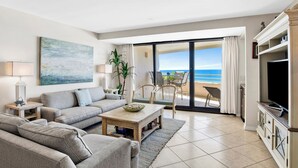 Ein modernes Wohnzimmer mit Sofa, Couchtisch und Fernseher, das zu einem Balkon mit Blick auf das Meer führt.