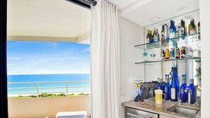 Ein Balkon mit Meerblick, eine Bar mit verschiedenen Flaschen und eine Sitzecke mit einem Stuhl.