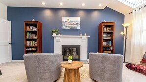 A living room with two grey armchairs, a round wooden coffee table, a white fireplace, and two bookshelves with books. - 4BR Family Retreat Near Annapolis w/ Large Yard (Annapolis)