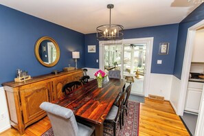 Une salle à manger avec une table en bois, des chaises, un lustre et un miroir au mur.