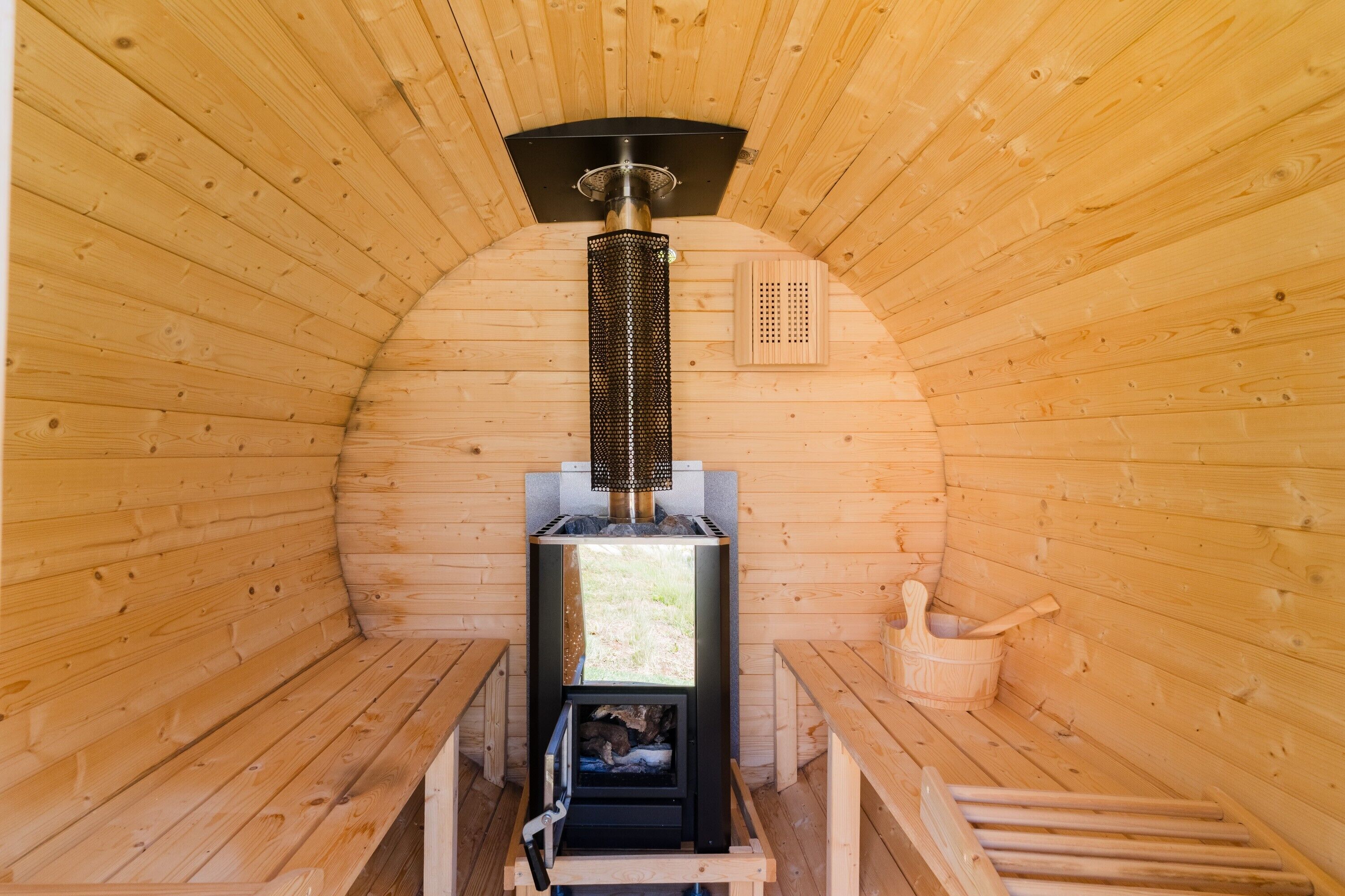 A sauna with wooden walls, a bench, a heater, and a wooden bucket.