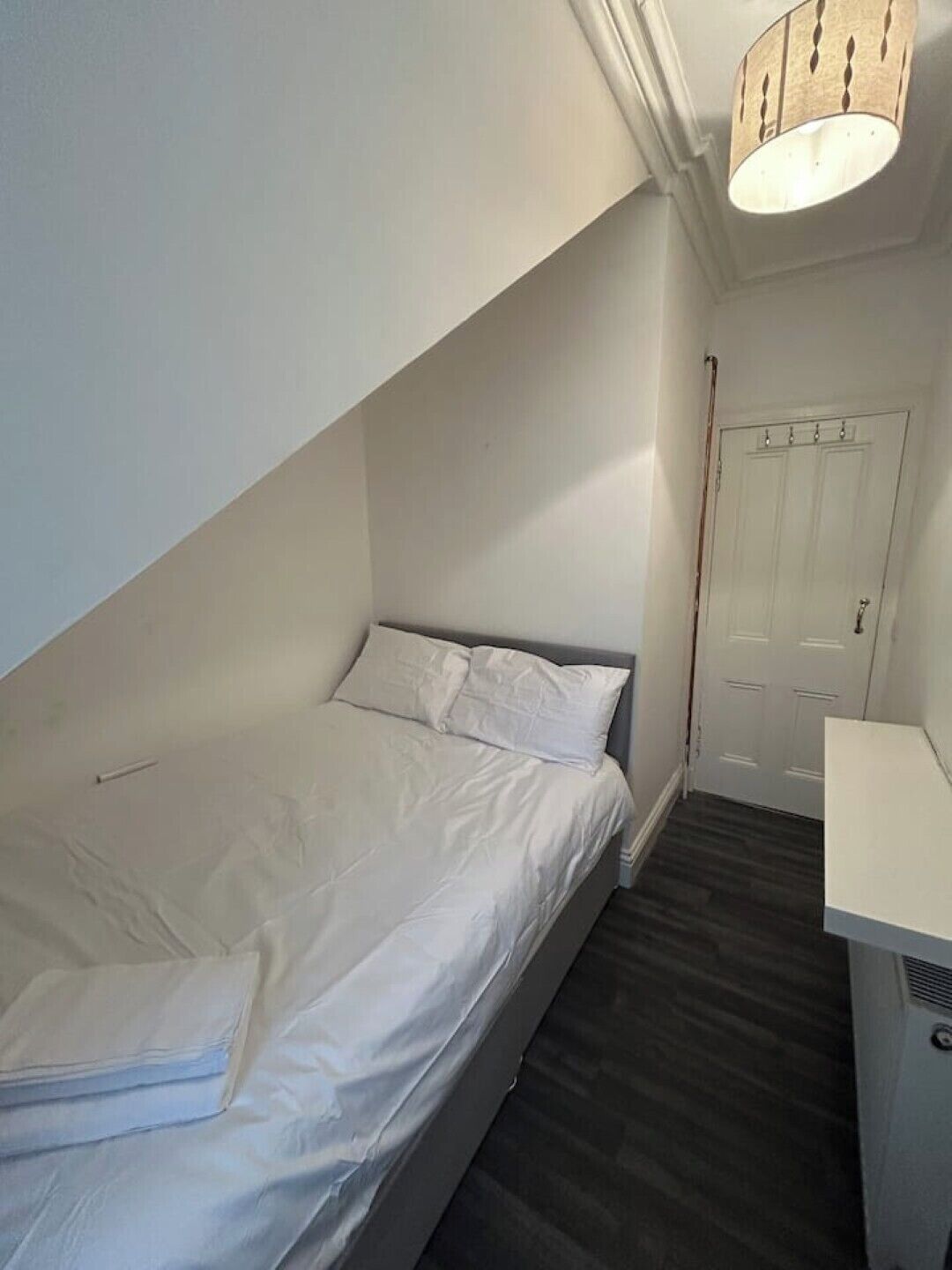 A small, neatly arranged bedroom with a single bed, a bedside table, and a door.